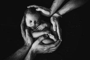 grayscale photo of hands holding a baby