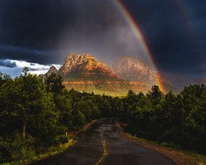 A rainbow appears over a road with a mountain in the background