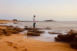 man in white shirt standing on brown sand near body of water during daytime