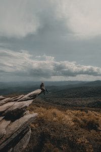 person sitting on edge of brown cliff