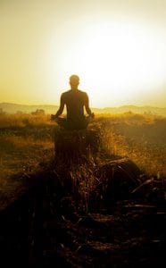 man meditating with the sun rising in the background
