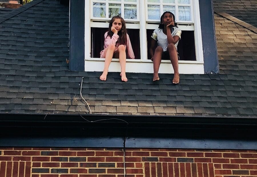 two girls sitting on white 2-panel windows during daytime